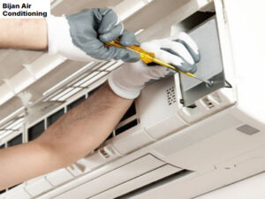 A technician performing maintenance on an indoor AC unit for Bijan Air-Conditioning in Chandler, AZ