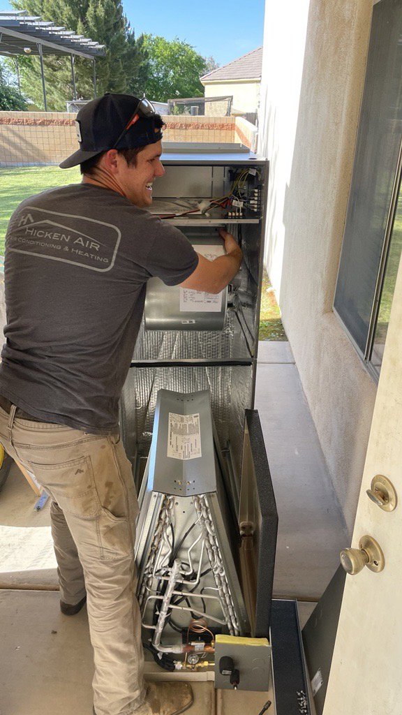 A Hicken Air technician working on the internal components of an indoor HVAC air handler unit in Gilbert, AZ