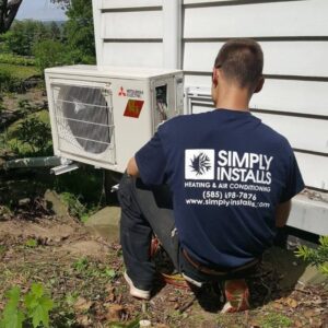 A Simply Installs Heating & Air Conditioning technician working on an outdoor Mitsubishi Electric HVAC unit in Shortsville, NY.