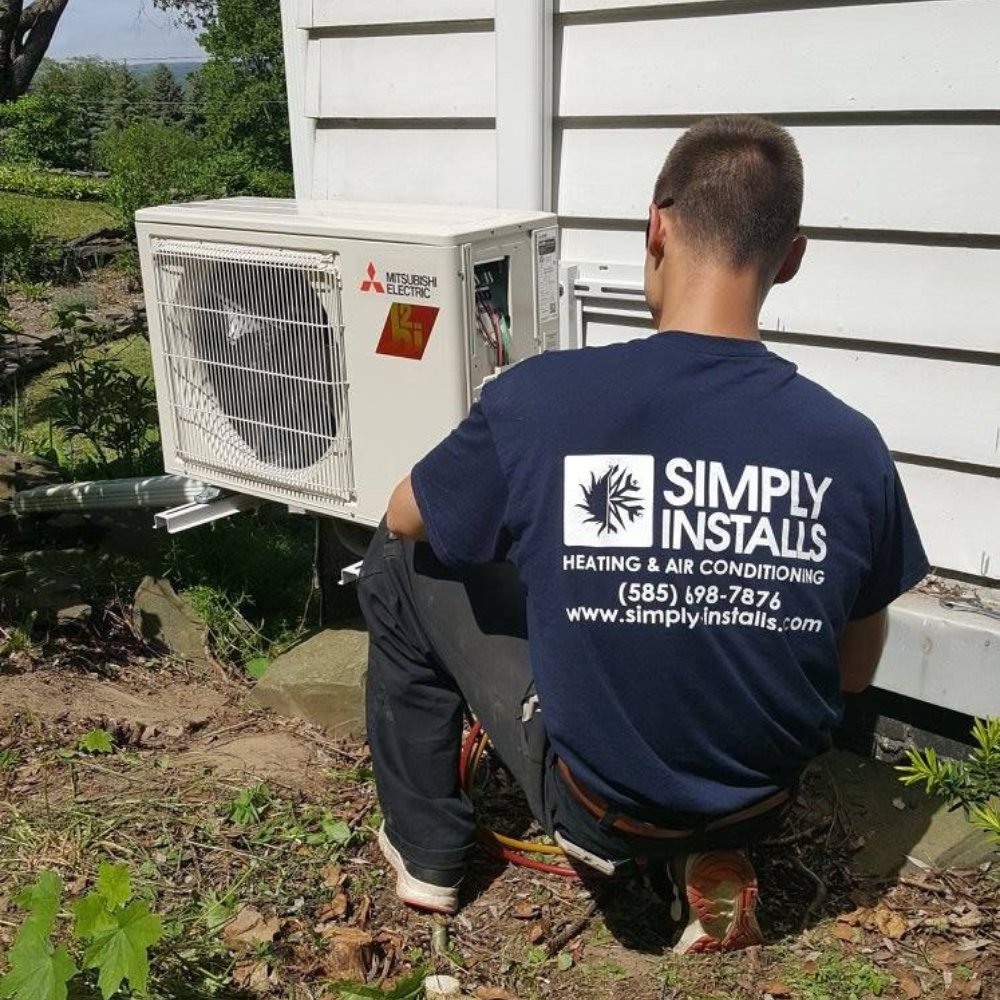 A Simply Installs Heating & Air Conditioning technician working on an outdoor Mitsubishi Electric HVAC unit in Shortsville, NY.