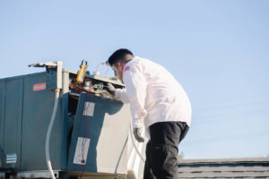 A technician working on a rooftop HVAC unit, inspecting components for A/C Valley, LLC in Tempe, AZ.