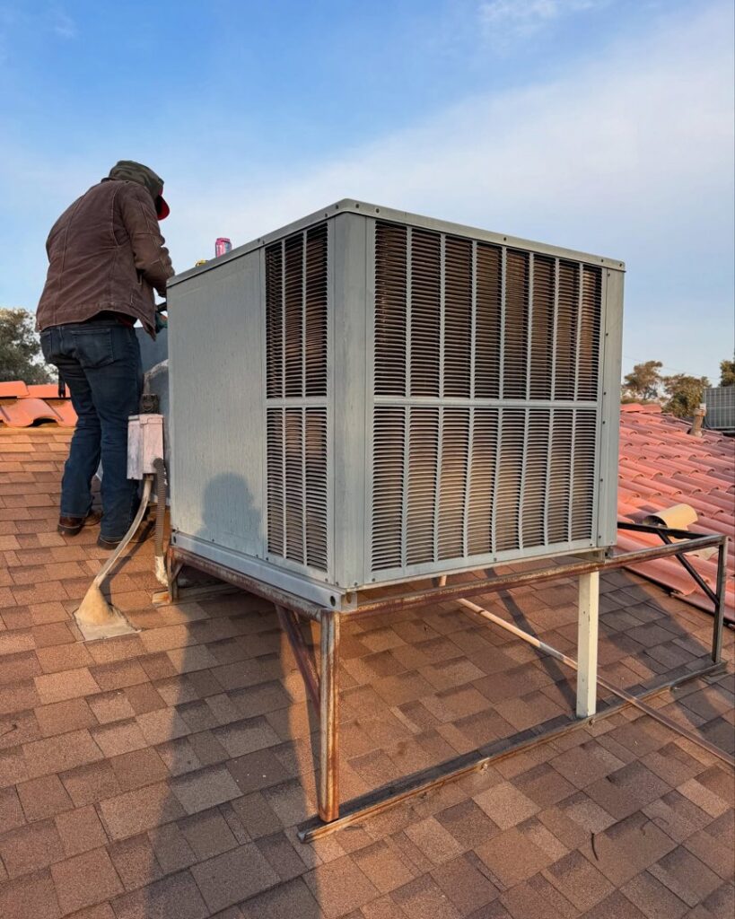 A technician performing service on a rooftop HVAC unit on a tiled roof by Cool Camel HVAC in Henderson, NV