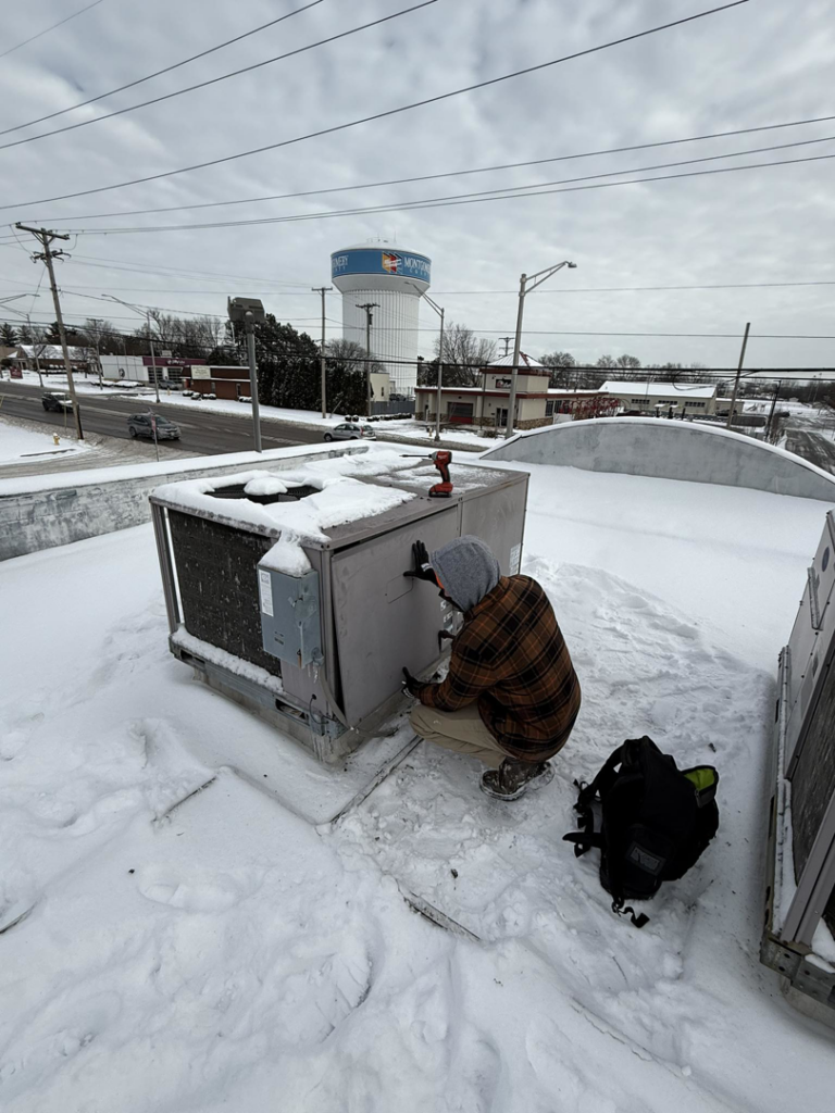 A technician performing maintenance on a rooftop HVAC unit covered in snow for Direct Service HVAC & Maintenance in Lewisburg, OH.