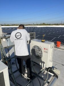 A technician working on a rooftop mini-split HVAC outdoor unit with solar panels for 365 Mechanical in Mesa, AZ.