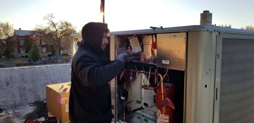 A technician performing maintenance on a large rooftop HVAC unit for Frederick Plumbing, Heating & Air Conditioning in Wichita, KS