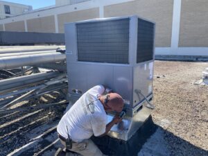 A technician from Total Living Comfort performing maintenance on a commercial rooftop HVAC unit in Irvington, AL.