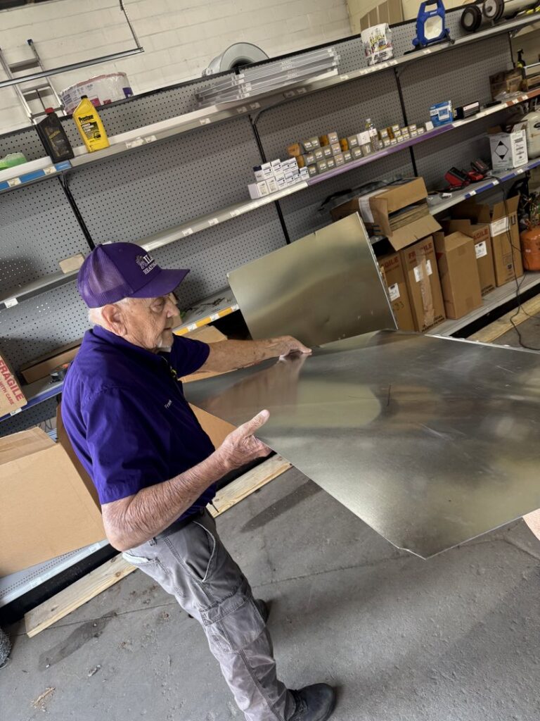 An experienced Milan Heating & Air technician working with a large sheet of metal for ductwork fabrication in Milan, TN.