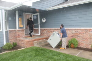 Two technicians carrying a new furnace into a residential home for Frederick Plumbing, Heating & Air Conditioning in Wichita, KS