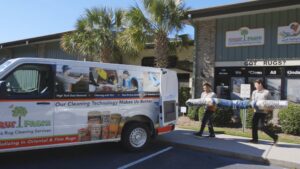 Two technicians carrying a rolled rug to a service van for Carpet & Rug Cleaning in Mount Pleasant, SC.