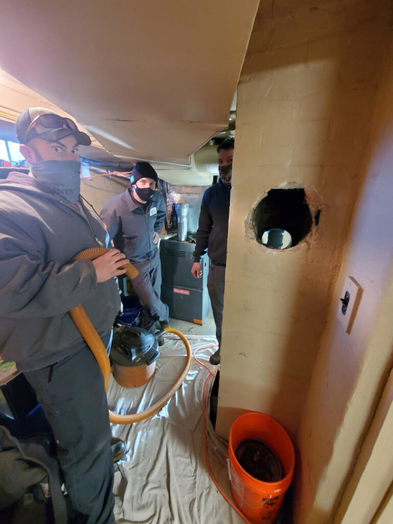 Midtown Chimney Sweeps technicians cleaning a furnace vent or chimney flue in a utility room in Golden, CO.