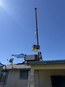 Technicians on a roof guiding an HVAC unit being lowered by a crane for Ash Cooling & Heating in Mesa, AZ.