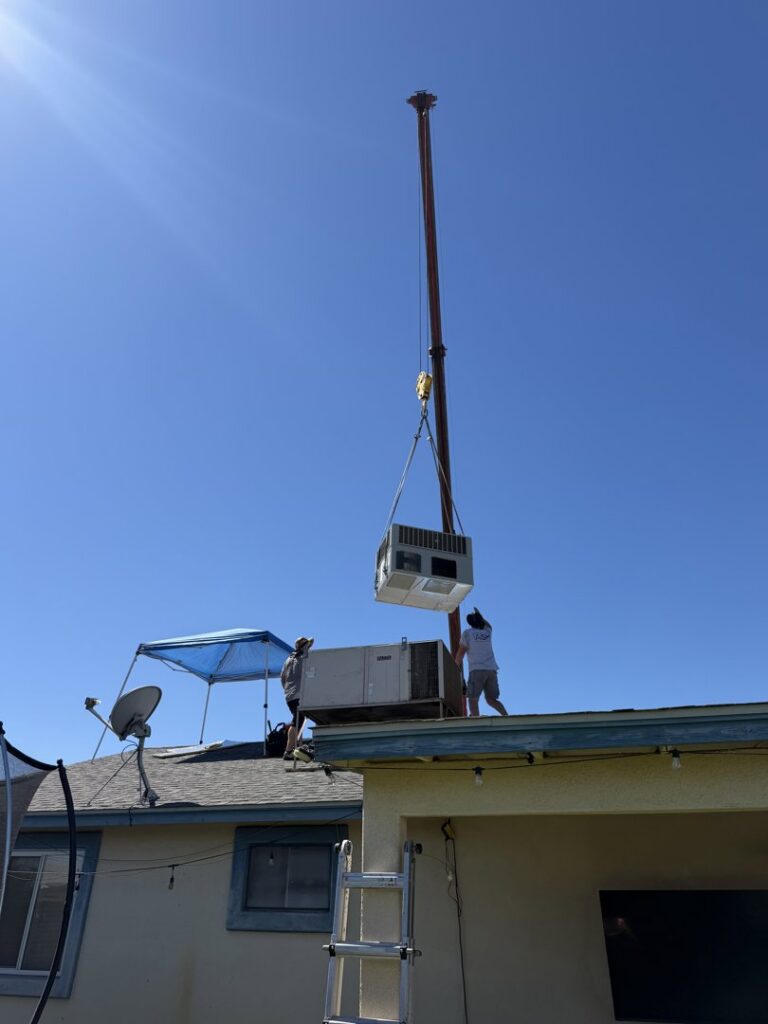 Technicians on a roof guiding an HVAC unit being lowered by a crane for Ash Cooling & Heating in Mesa, AZ.