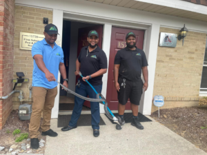 Three technicians from First Solutions Pest & Home Services holding a captured snake with a tong in Derwood, MD
