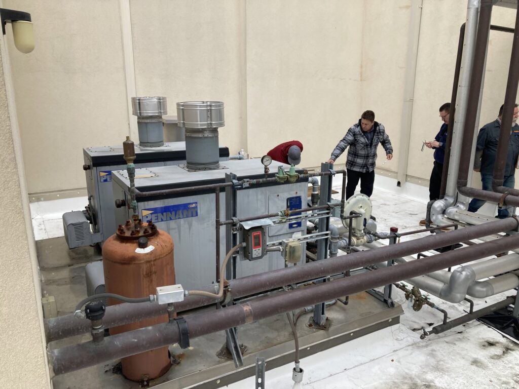 Technicians inspecting large industrial HVAC units on a rooftop for Hurn Mechanical Heating & Cooling in El Cajon, CA.