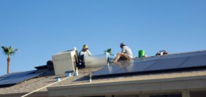 Two technicians installing ductwork on a residential roof with solar panels for Ash Cooling & Heating in Mesa, AZ.