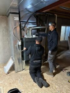 Two Fix It Now Heating and Cooling technicians installing or servicing an indoor furnace unit in Thornton, CO