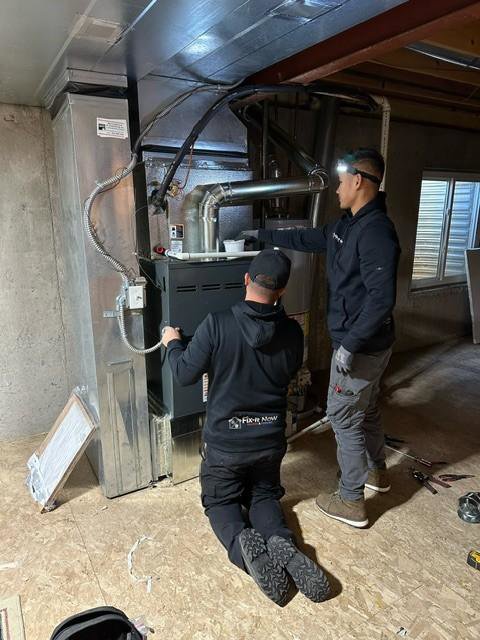 Two Fix It Now Heating and Cooling technicians installing or servicing an indoor furnace unit in Thornton, CO