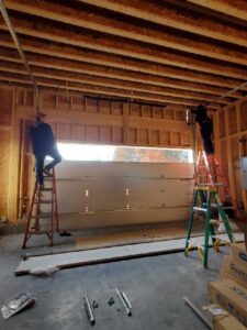 Two technicians on ladders installing a garage door in a new construction frame by Door Serv Pro in Inwood, WV.