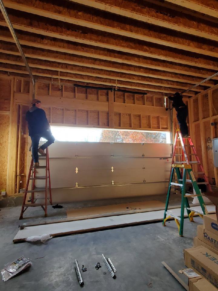 Two technicians on ladders installing a garage door in a new construction frame by Door Serv Pro in Inwood, WV.