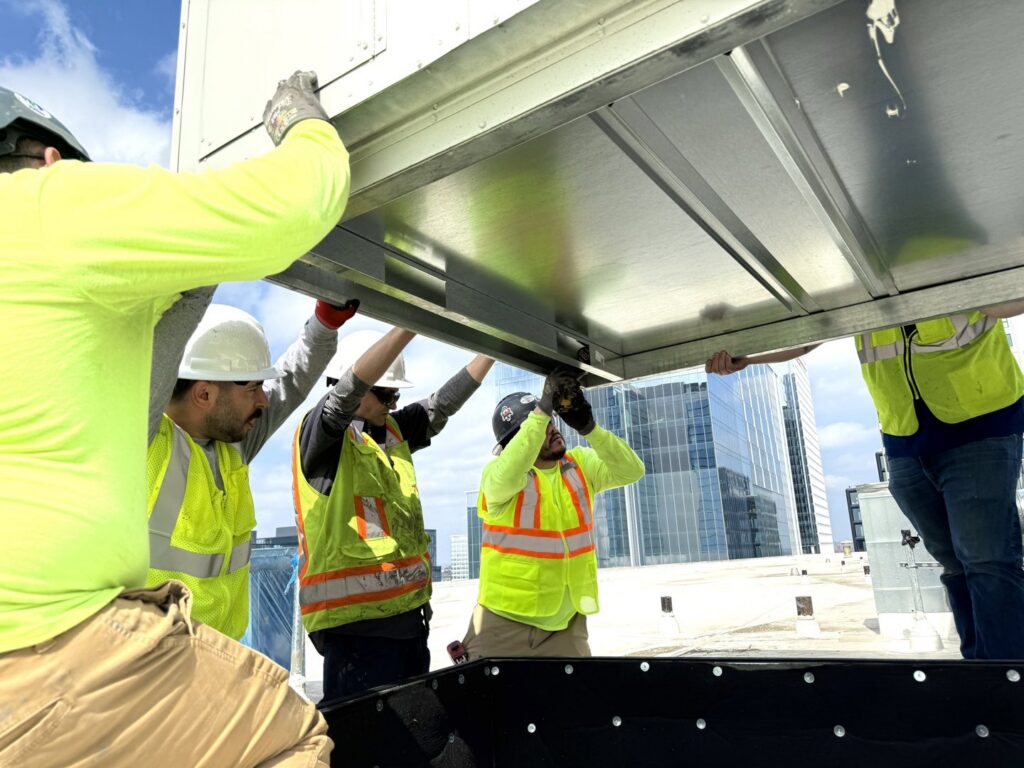 Interstate AC technicians installing HVAC ductwork or a component on a rooftop with city buildings in the background in Nashville, TN.