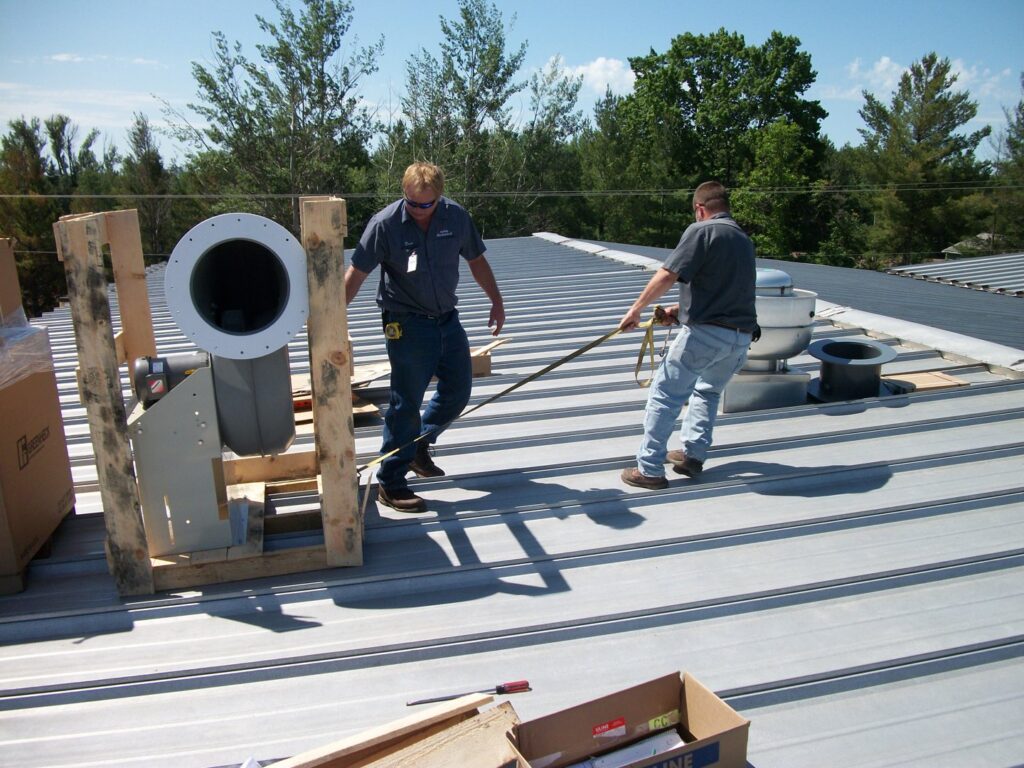 Two technicians from Action Mechanical LLC installing a new HVAC unit on a commercial roof in Eau Claire, WI.