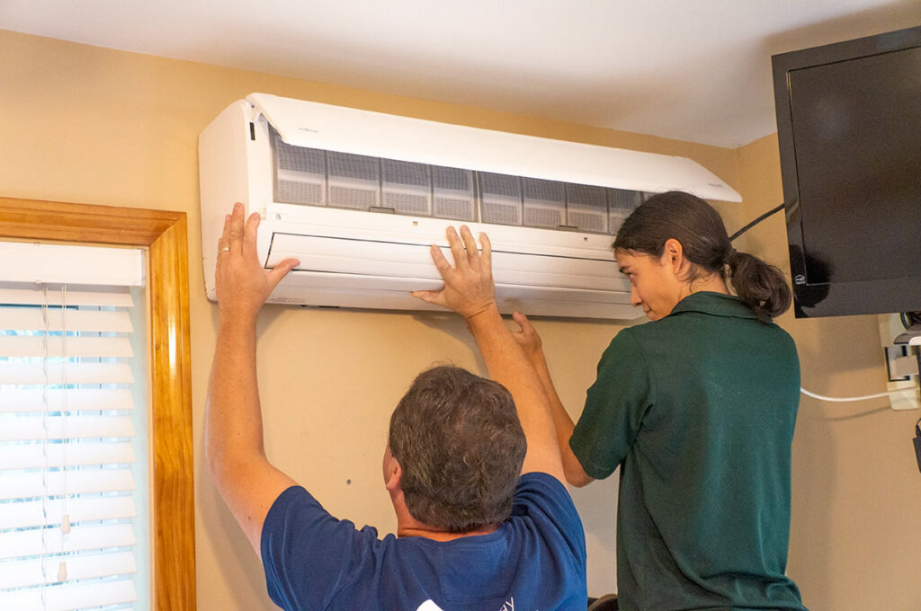 Two technicians installing an indoor mini-split HVAC unit for HomeWorks Energy in Medford, MA.