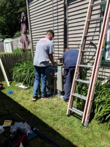 Two technicians from Total Comfort Heat and Air Conditioning, Inc. installing an outdoor mini-split unit in Rochester, NY.