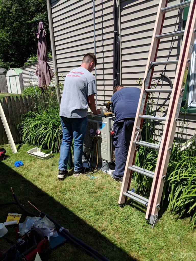 Two technicians from Total Comfort Heat and Air Conditioning, Inc. installing an outdoor mini-split unit in Rochester, NY.