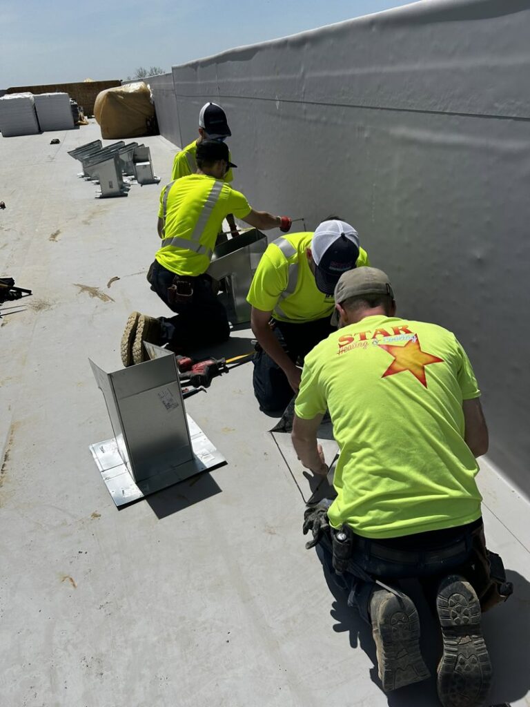Technicians from STAR Heating Cooling Plumbing installing metal flashing and vents on a commercial rooftop in Fishers, IN.