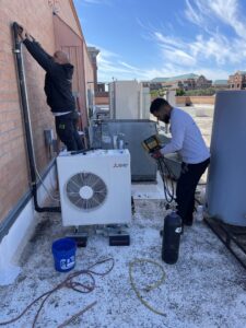 Two technicians installing a rooftop mini-split HVAC system, connecting lines and gauges for 365 Mechanical in Mesa, AZ.