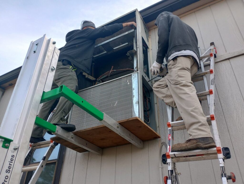 Two HVAC technicians on ladders installing a wall-mounted heating and cooling unit for HP Mechanical LLC in Santa Rosa, CA.