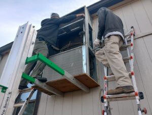 Two HVAC technicians on ladders installing a wall-mounted heating and cooling unit for HP Mechanical LLC in Santa Rosa, CA.