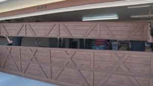Two technicians from Iconic Garage Door Service installing a new wooden-style garage door panel in Queen Creek, AZ