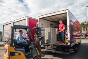 Two technicians loading an outdoor HVAC unit onto a company truck with a forklift for Parks Heating Cooling Plumbing & Electrical in Indian Trail, NC