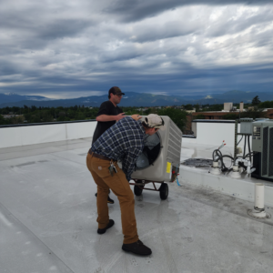 Two technicians moving a new rooftop AC unit with a dolly for JL Mechanical in Pleasant Grove, UT.