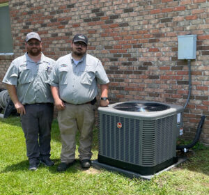 Two technicians standing proudly next to a newly installed Rheem outdoor AC unit by Total Living Comfort in Irvington, AL.