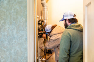 Two HVAC technicians performing repairs on an indoor furnace or air handler unit for Comfort Engineering Co Inc in Tupelo, MS