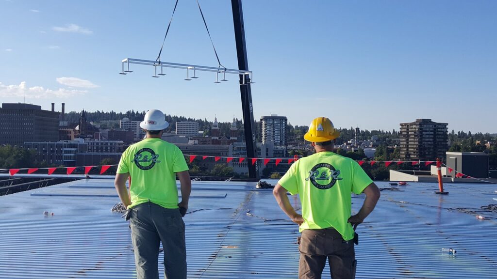 R&R Heating & Air Conditioning technicians on a rooftop overseeing the lift of HVAC equipment in Spokane, WA.