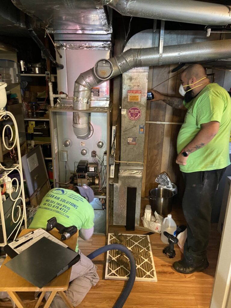 Two Clean Air Solutions technicians servicing a furnace unit in a basement in Gaithersburg, MD.