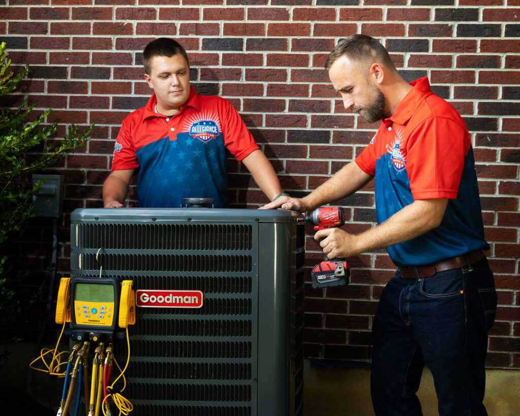 Two Allegiance Heating & Air technicians servicing a Goodman outdoor AC unit in Greenville, IN.
