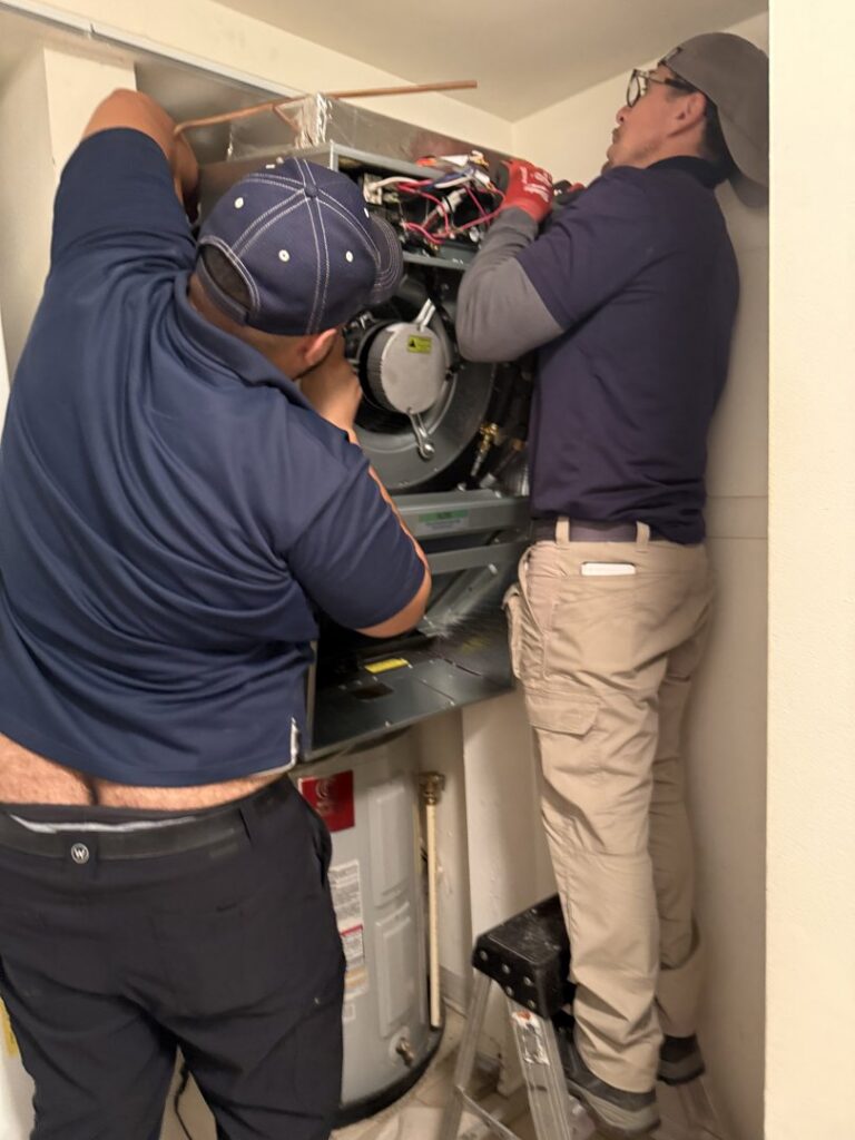 Two Residential Express Heating & Air technicians servicing an indoor HVAC unit in Sterling, VA.