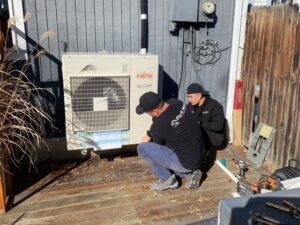 Two Fix It Now Heating and Cooling technicians servicing an outdoor mini-split HVAC unit in Thornton, CO
