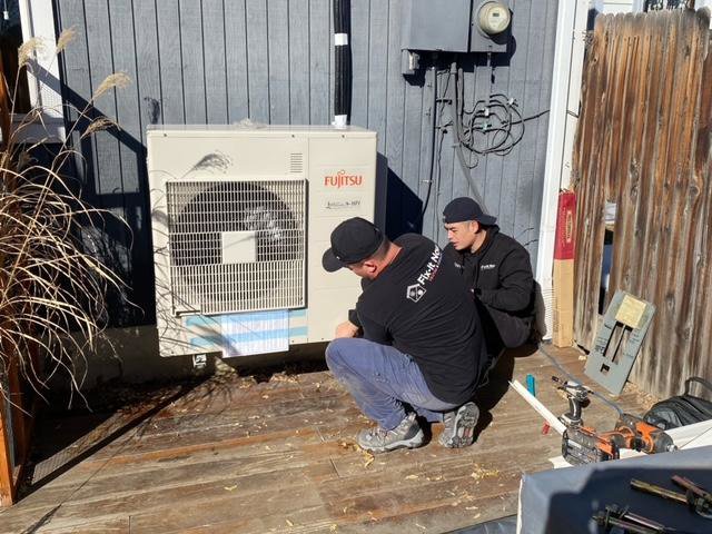 Two Fix It Now Heating and Cooling technicians servicing an outdoor mini-split HVAC unit in Thornton, CO