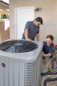Two Modern Air Conditioning & Heating technicians servicing an outdoor AC unit in Boulder City, NV.