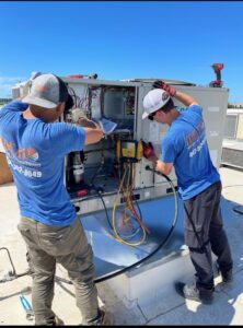 Two technicians servicing a commercial rooftop HVAC unit for Ideal Heating & Air Conditioning in Omaha, NE.