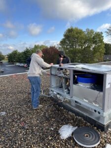 Two technicians from STAR Heating Cooling Plumbing servicing a large commercial rooftop HVAC unit in Fishers, IN.