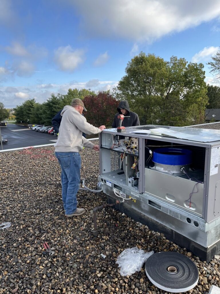 Two technicians from STAR Heating Cooling Plumbing servicing a large commercial rooftop HVAC unit in Fishers, IN.