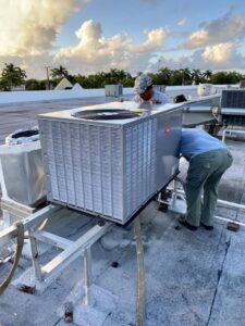 Two technicians performing service on a large rooftop HVAC unit for T&D Air Conditioning in Fort Lauderdale, FL.