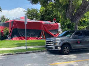 Technicians setting up a red and black fumigation tent around a house by PNP Pest Solutions LLC in Miami, FL.