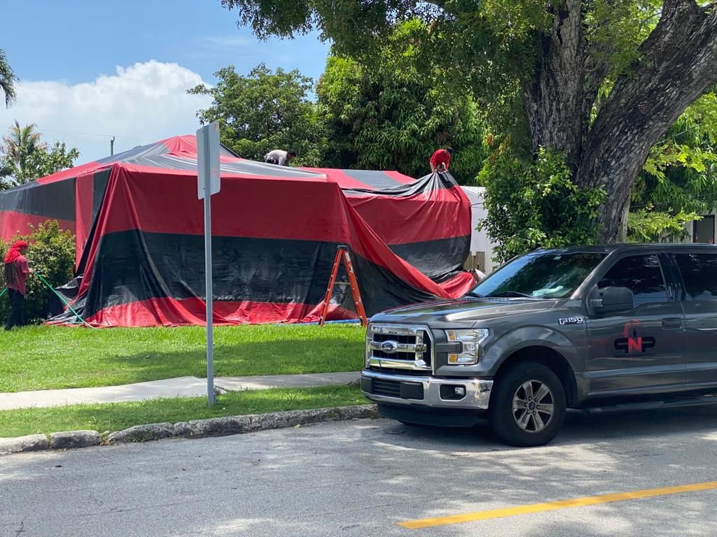 Technicians setting up a red and black fumigation tent around a house by PNP Pest Solutions LLC in Miami, FL.